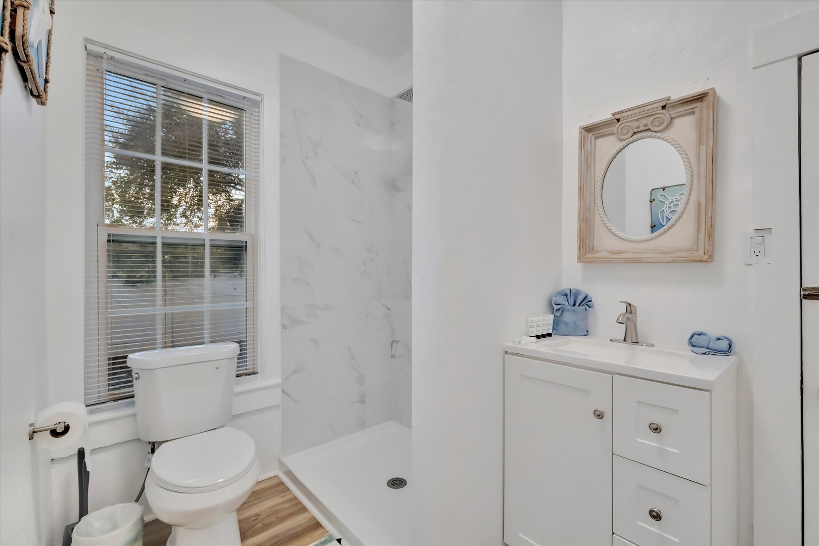 Your private bathroom blends sleek marble-style walls with coastal-inspired touches. Natural light pours in, highlighting the modern vanity and spacious walk-in shower designed for your comfort.