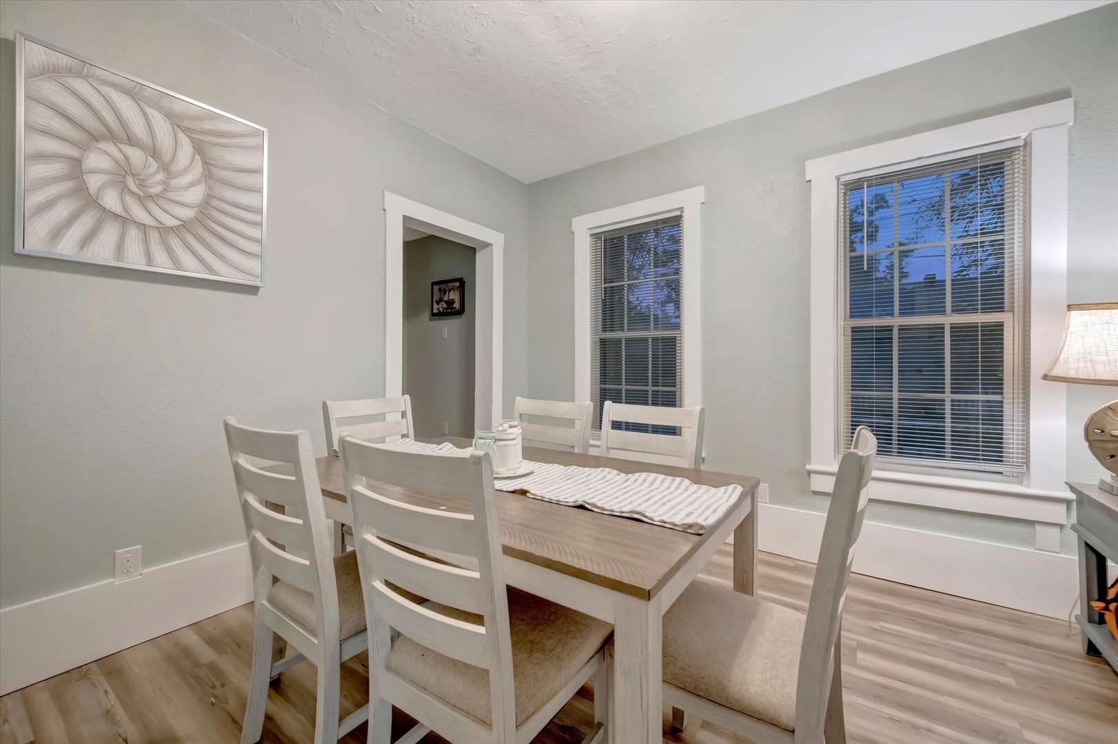 Gather around this inviting dining table, where morning coffee meets sunset dinners. Soft coastal tones and natural light through tall windows create a relaxed setting for your vacation meals together.