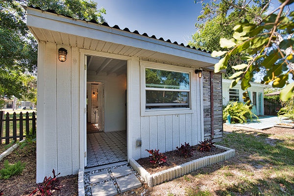 The charming entrance to your cottage welcomes you with a clean, bright facade, cozy lighting, and lush green surroundings—your peaceful retreat awaits just beyond the door.