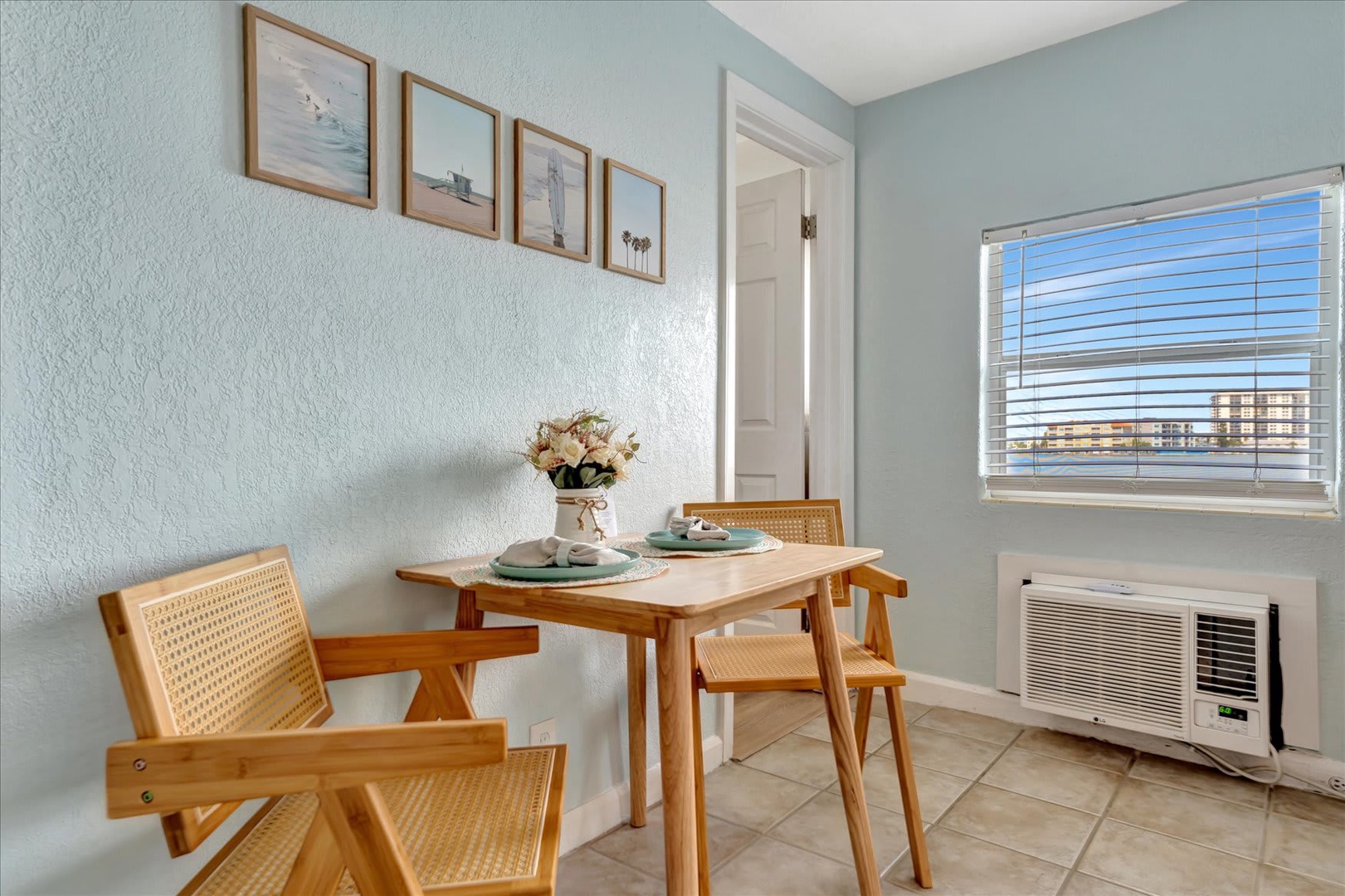Bright, airy dining nook with soft coastal blues and warm wood tones. Natural light floods through the window, creating the perfect setting for morning coffee or evening meals.