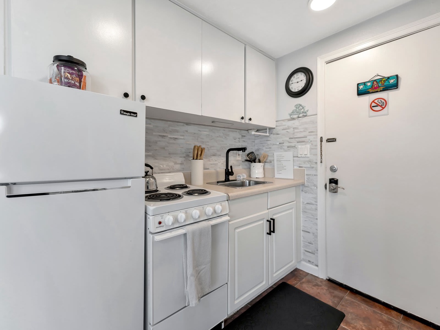 Your fully equipped kitchenette has everything you need to prepare meals, with bright white cabinetry, modern stone backsplash, and a cozy layout perfect for cooking at home.