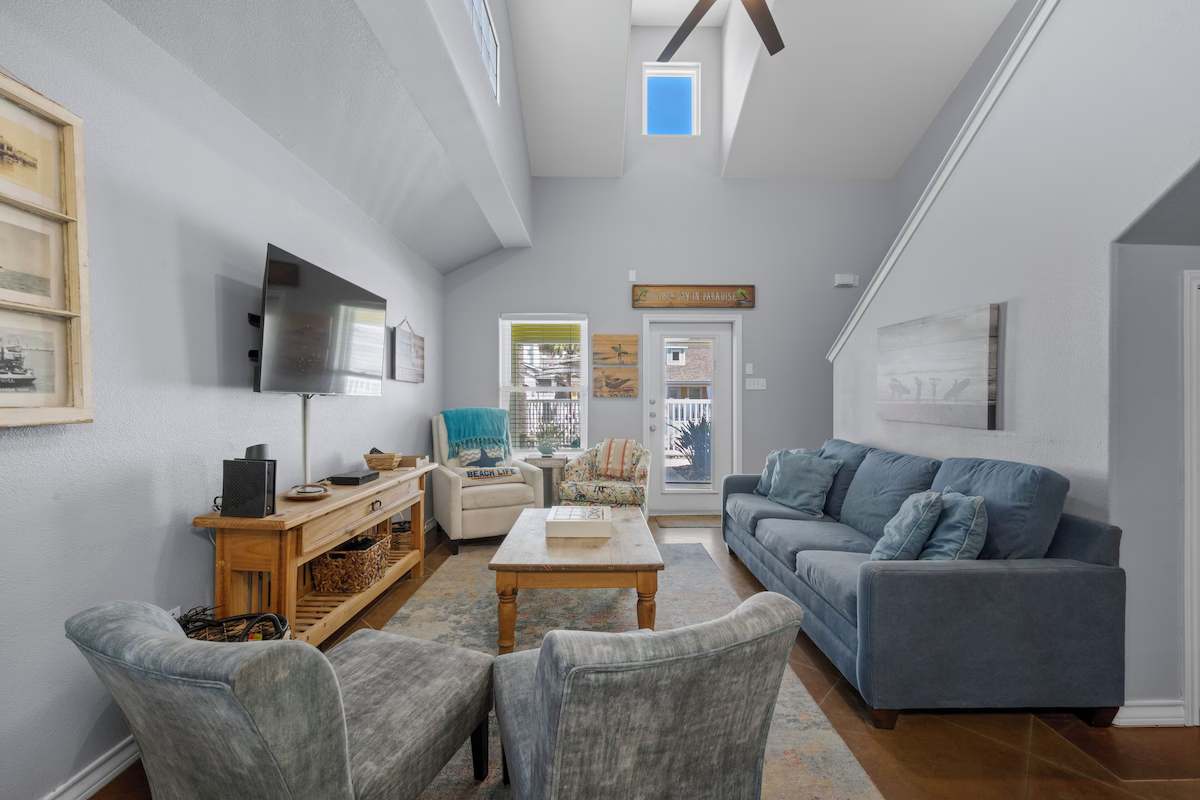 Relax in your spacious living room with soaring ceilings and abundant natural light streaming through the skylight, where coastal-inspired decor and plush seating create a peaceful retreat after a day of adventures.