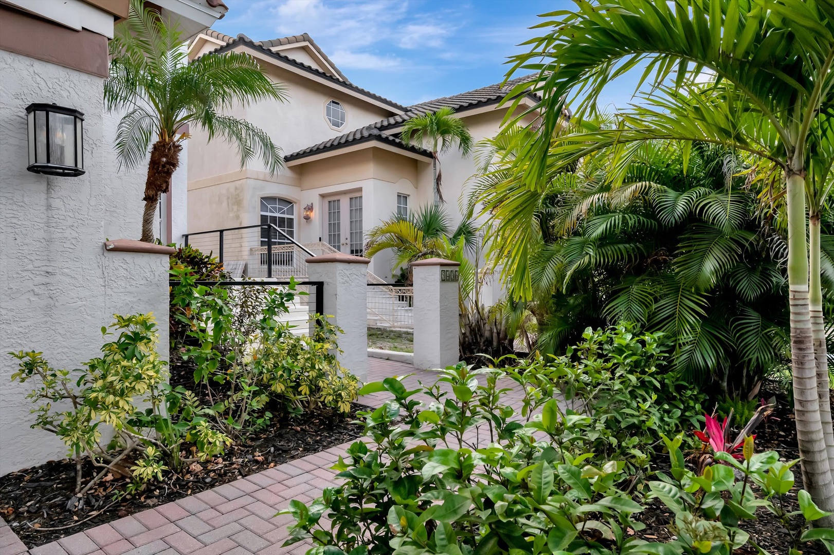 A beautiful Mediterranean-style property welcomes you with lush tropical landscaping featuring vibrant palms and flowering plants. The elegant stucco facade, tiled roof, and private front courtyard create an inviting arrival experience.