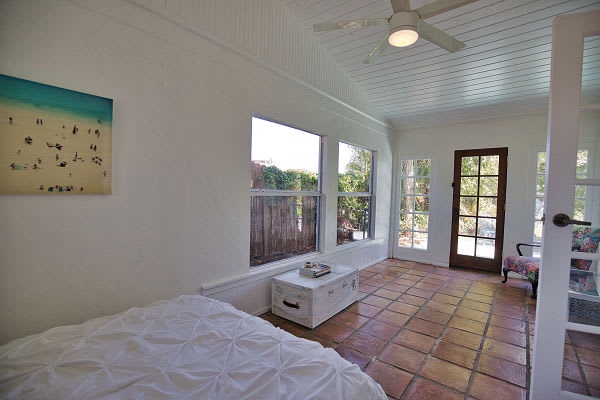 Drift off to sleep in this sun-filled bedroom, where natural light pours through large windows and French doors open to your private outdoor retreat. A ceiling fan keeps you cool, and the charming terracotta floors add warmth and character.