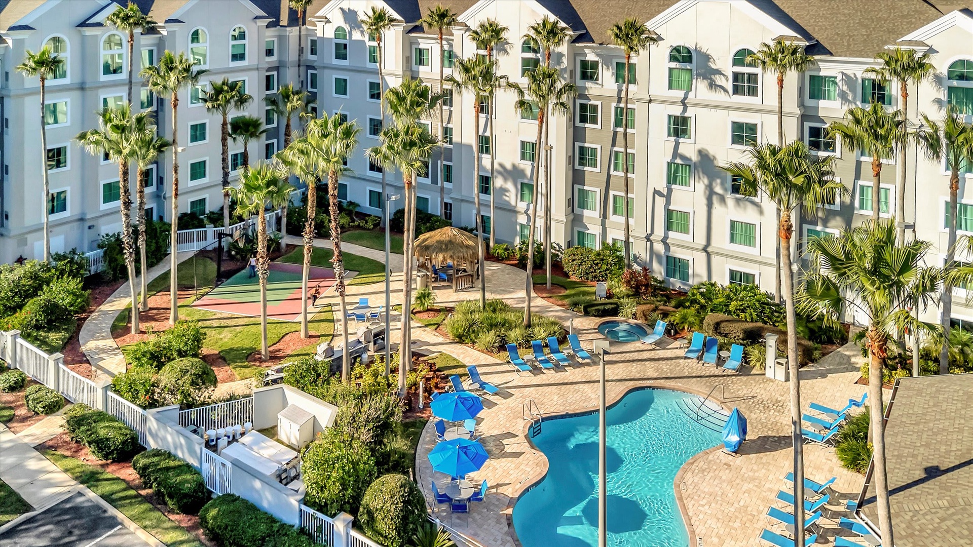 An aerial view captures the resort's welcoming courtyard, featuring a sparkling pool, tropical palms, and vibrant lounge chairs perfect for sunny days.