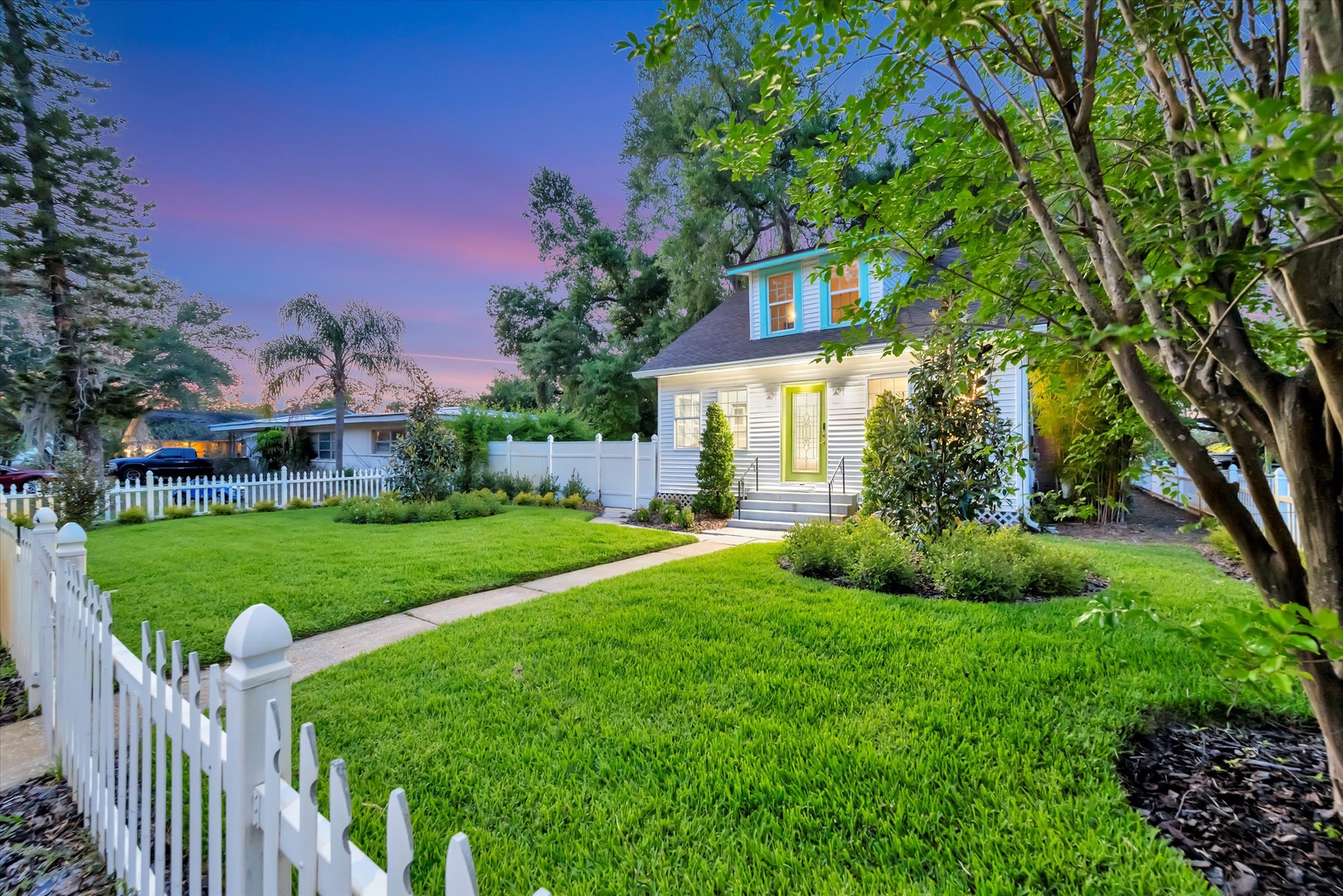 A charming cottage with a welcoming front entrance nestled in a peaceful residential setting. Lush landscaping and mature trees frame the property at dusk, offering a tranquil arrival experience.