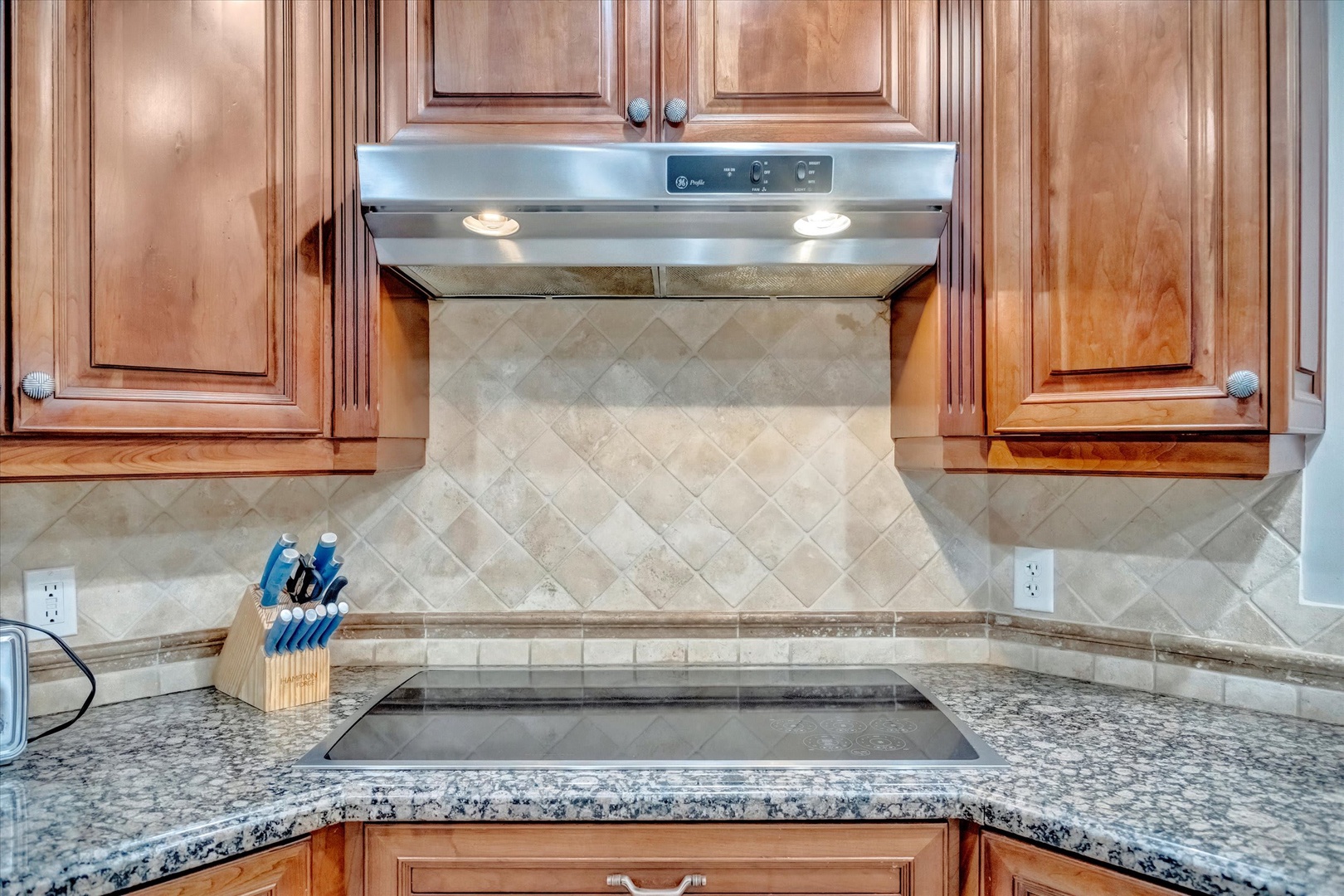 This fully equipped kitchen features elegant granite countertops, custom wood cabinetry, and modern appliances including a sleek cooktop—perfect for preparing your favorite meals during your stay.