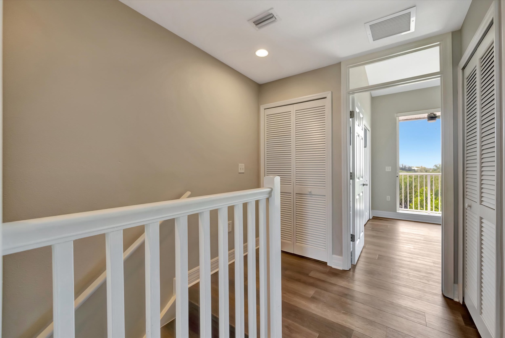 Step into your peaceful upstairs hallway, where warm hardwood floors guide you toward bright, sun-filled spaces and your own private balcony retreat with inviting outdoor views.