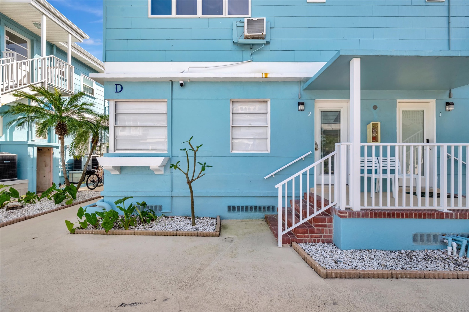 Charming coastal building with inviting blue exterior and tropical landscaping, located in a beach neighborhood with easy access to nearby properties.