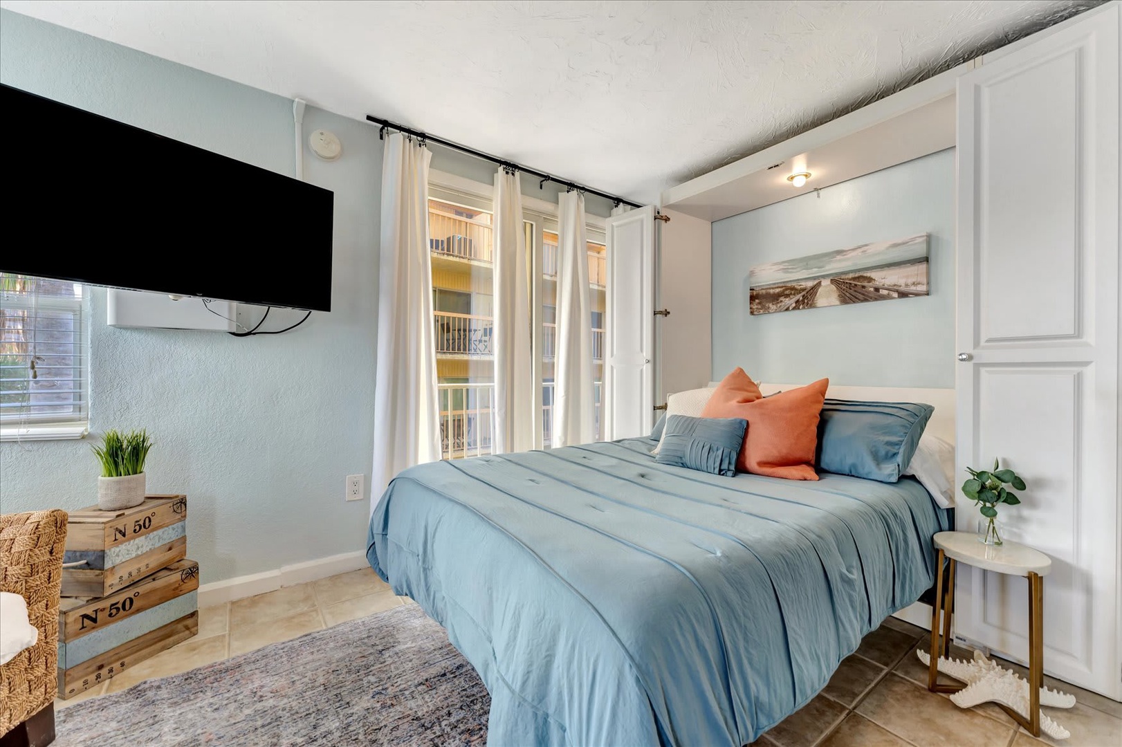 Sink into plush bedding in your serene bedroom, where soft blues and warm coral accents create a peaceful retreat. Watch your favorite shows on the wall-mounted TV or unwind with views through the curtained doorway.