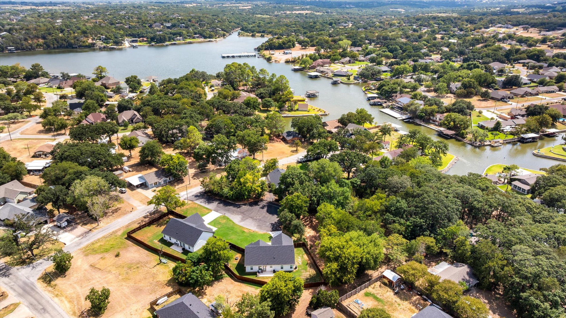 Lakeside residential community nestled among mature trees with scenic waterfront access and rolling Texas Hill Country beyond.