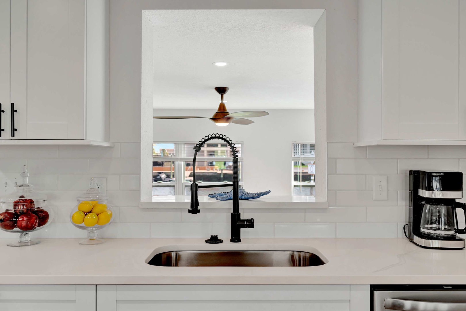 Step into your bright, modern kitchen where crisp white surfaces and a sleek matte-black faucet make meal prep a pleasure. Fresh fruit adds a cheerful pop of color to your counter space.
