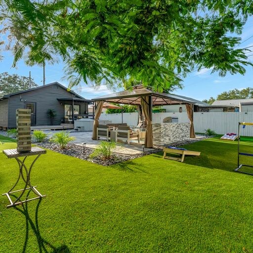 This beautifully landscaped backyard features a spacious covered gazebo with comfortable seating, a modern fire feature, and lush green lawn—perfect for outdoor gatherings and relaxation.
