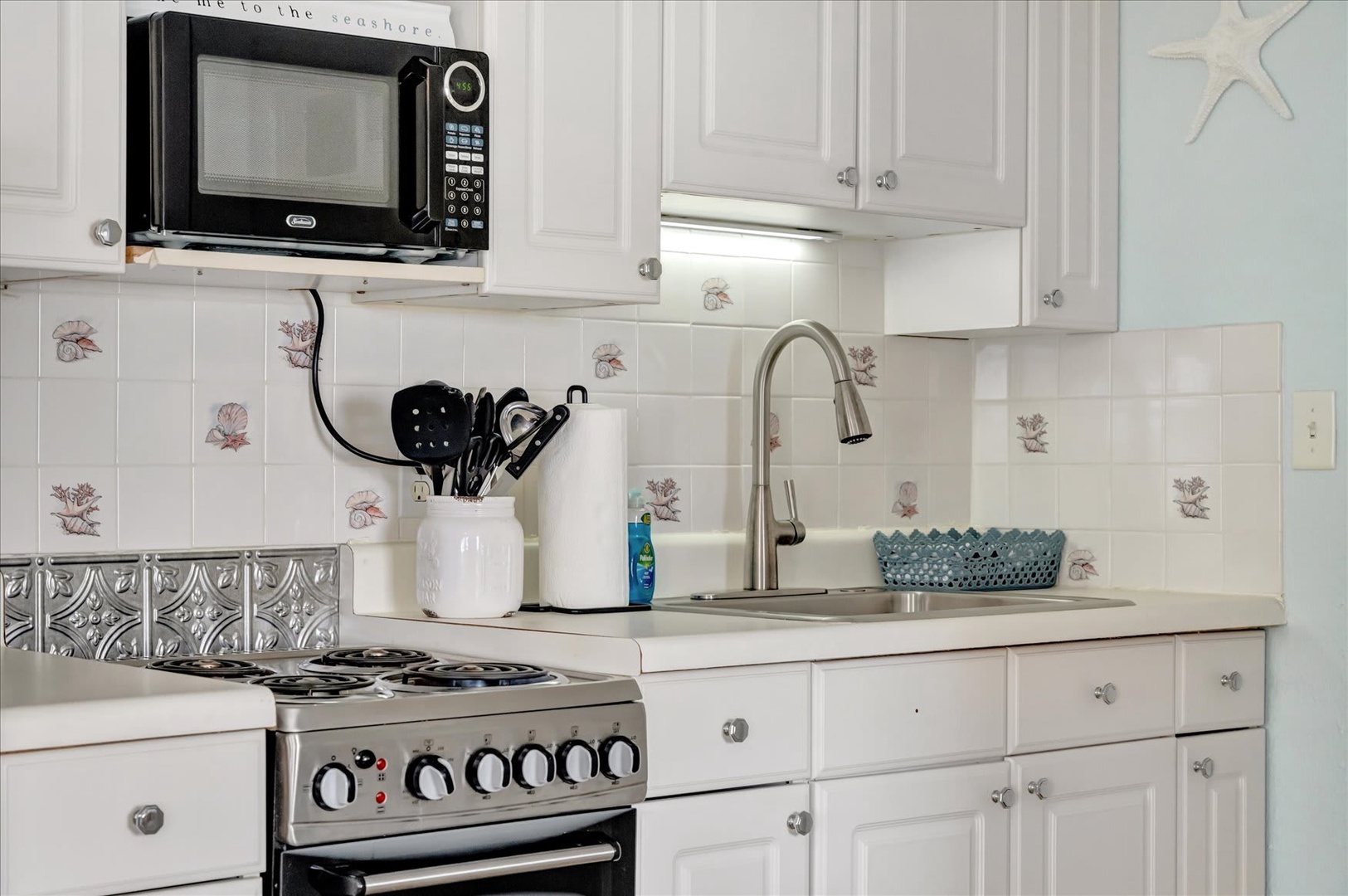 Fully equipped coastal kitchen with crisp white cabinetry and charming seashell-patterned tiles. Everything you need for beachside cooking adventures.