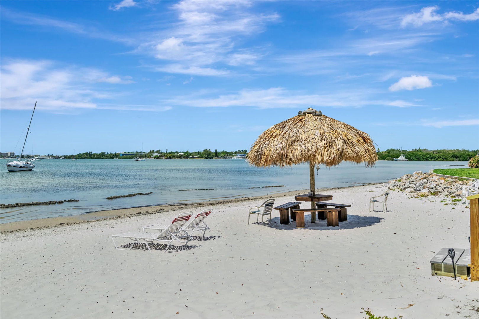 Private sandy beach with thatched palapa, lounge chairs, and picnic area along calm bay waters—your own slice of waterfront paradise.