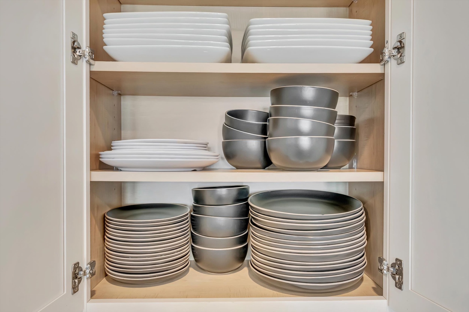 A fully stocked kitchen awaits, with fresh dishes and cookware neatly organized in the cabinet for your convenience.