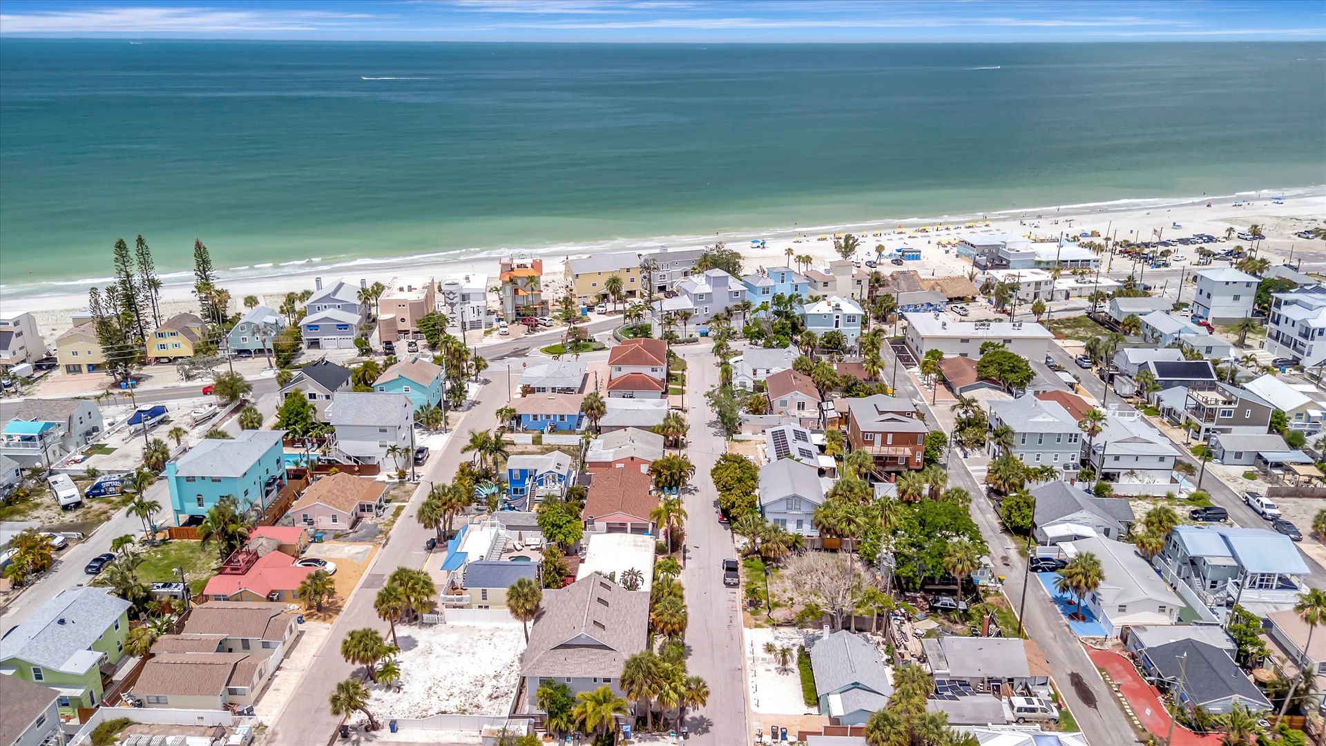 An aerial view of a vibrant beachside community with colorful homes nestled among palm trees, steps from white sandy shores and turquoise waters.