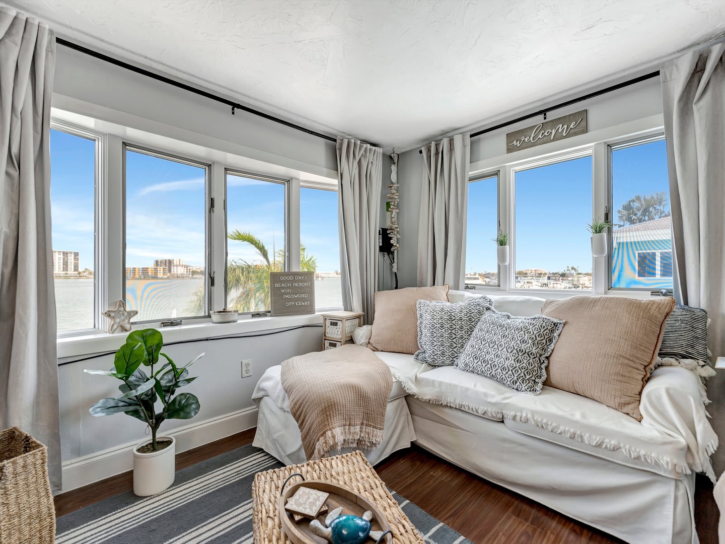 Sink into the plush daybed and let your gaze drift over the sparkling waterfront views. Sunlight floods this cozy nook through expansive windows, while soft textures and coastal decor invite you to relax and unwind completely.