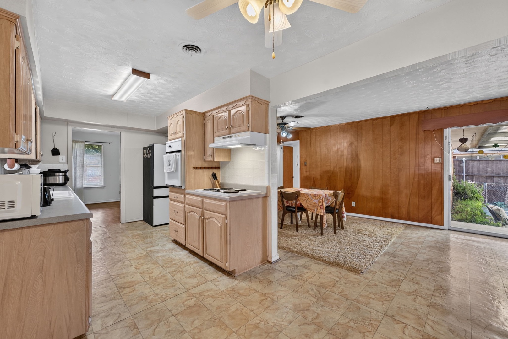 Spacious open-concept kitchen and dining area with warm wood tones, ample cabinetry, and natural light from large glass doors opening to your private backyard—perfect for easy entertaining and everyday comfort.