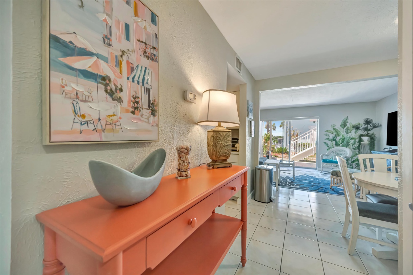 Bright, cheerful décor welcomes you with coastal charm—notice the playful orange console and tropical artwork setting a vacation vibe that flows all the way to the poolside patio beyond.