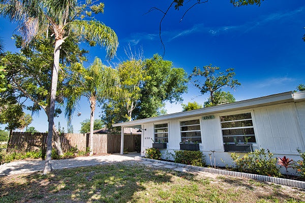 The property sits in a peaceful neighborhood, surrounded by lush tropical trees and backed by a bright blue sky—a welcoming retreat under the Florida sun.