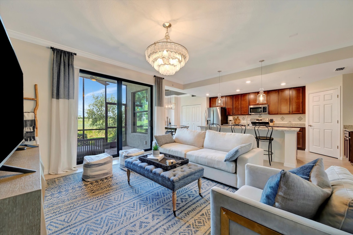 Settle into your open-concept living space, where a statement chandelier adds elegance overhead and thoughtfully chosen furnishings invite you to unwind. Natural light flows through the glass doors, framing serene views of the surrounding greenery.