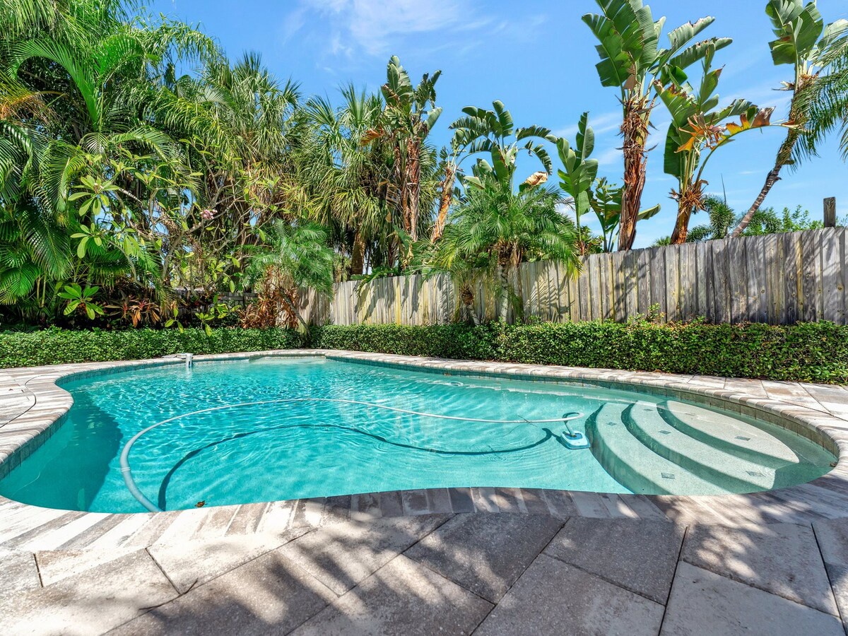 A sparkling pool awaits, surrounded by lush tropical palms and banana trees. Imagine lounging poolside in your private oasis, where warm sunlight filters through the greenery and built-in steps invite you to take a refreshing dip.