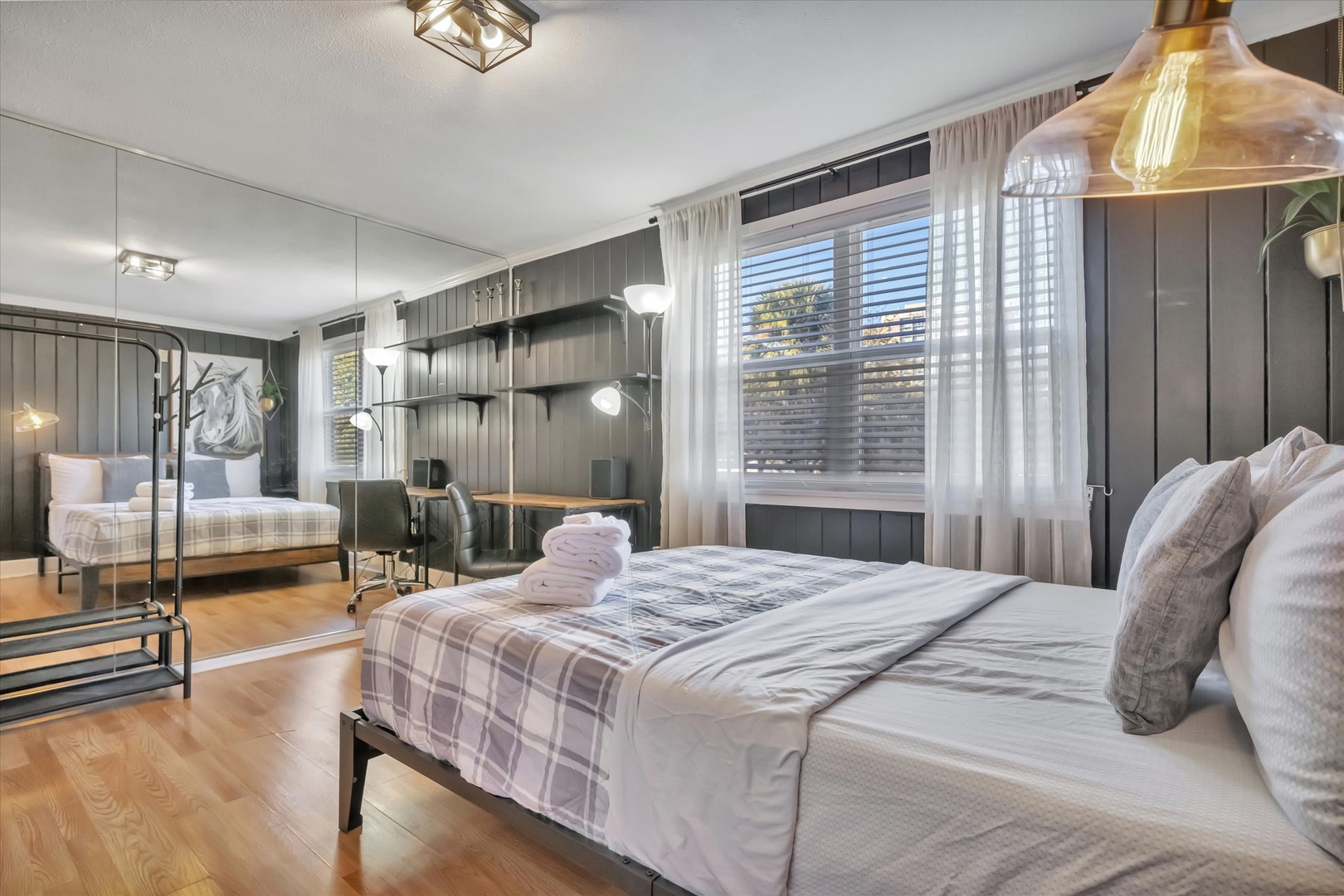 Your spacious bedroom features stylish plaid linens, warm wood floors, and natural light streaming through the windows—a peaceful retreat after exploring the area.