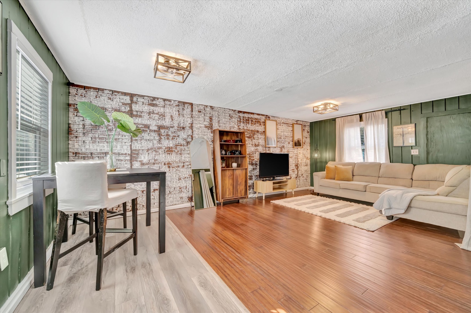 Sink into plush sectional seating in this stylish living space, where warm wood floors meet exposed brick accent walls and fresh greenery brings the room to life.