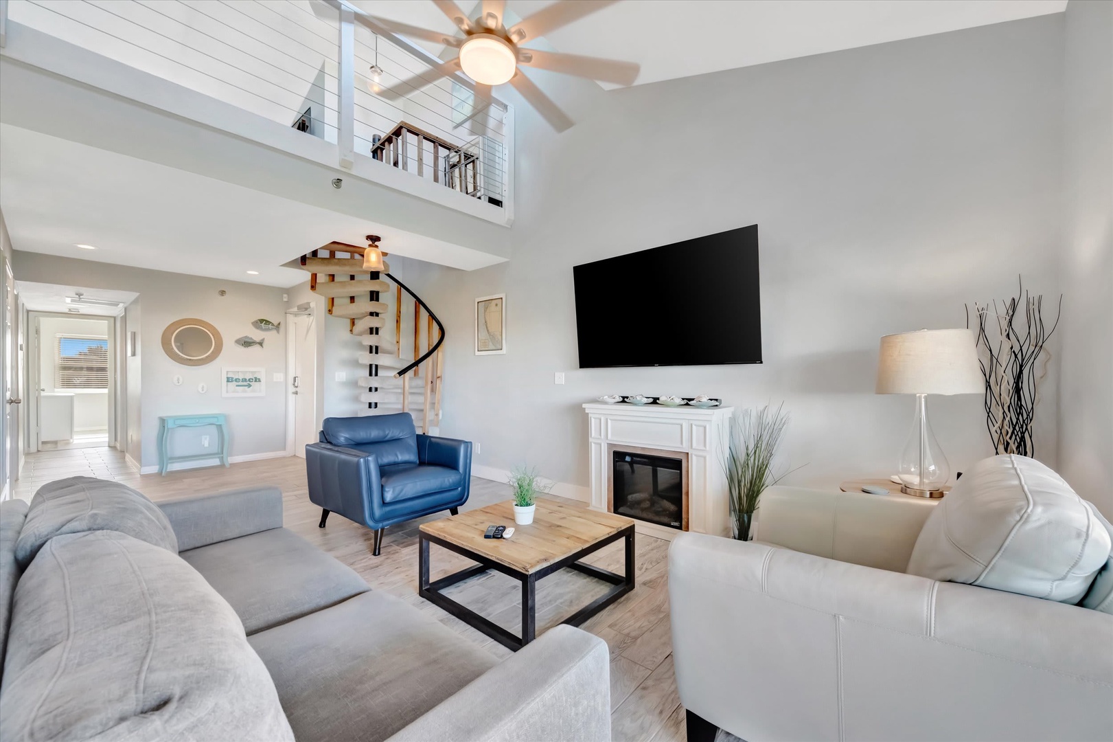 Relax in your bright, two-story living room with vaulted ceilings and coastal charm. Sink into plush seating, enjoy the fireplace, and feel the airy breeziness from the loft above.