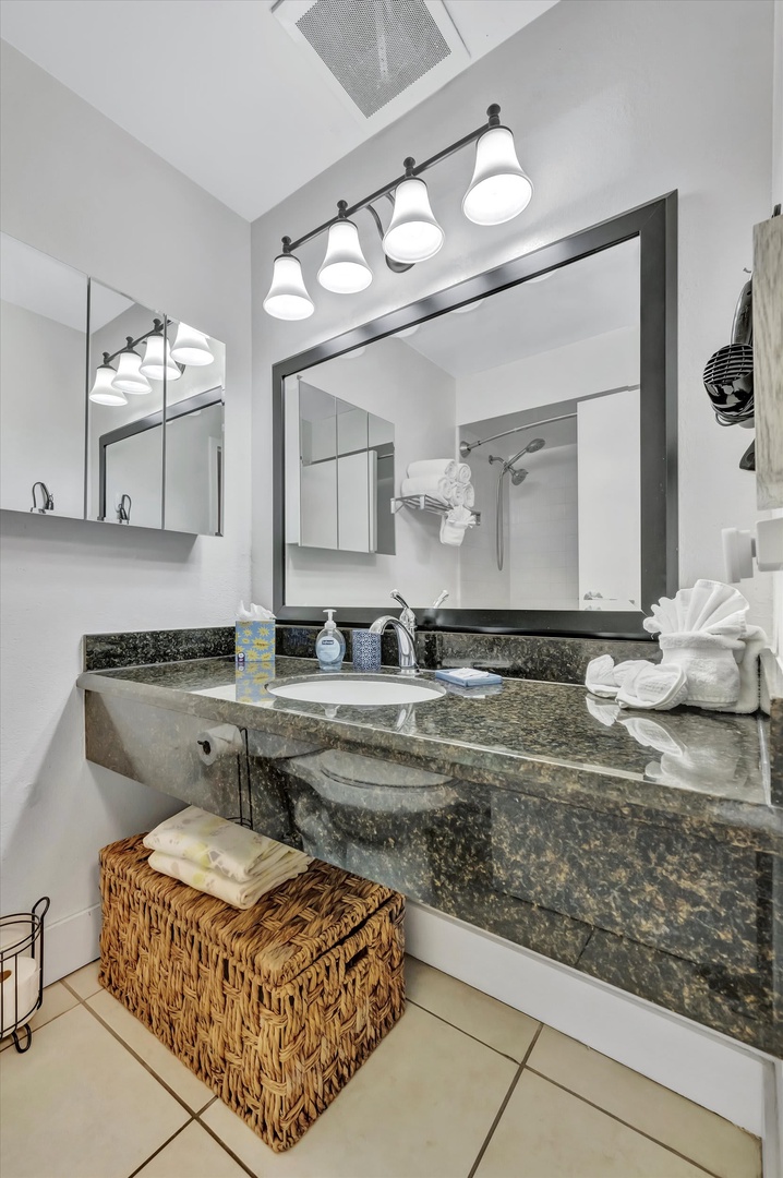 Step into your beautifully designed bathroom featuring a granite vanity, modern lighting, and fresh towels awaiting your arrival. The wicker basket adds a charming touch of coastal style.
