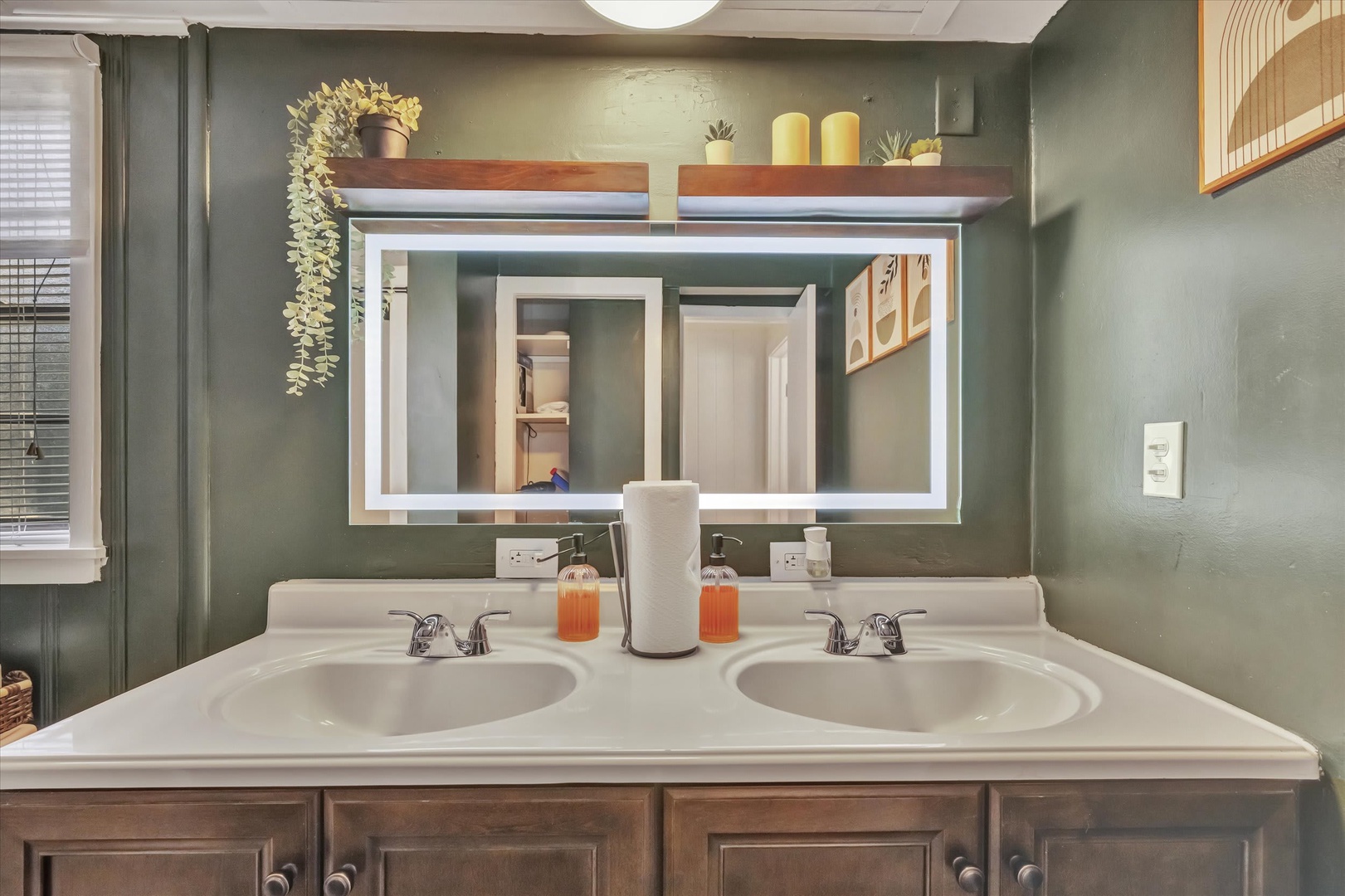 This dual-sink vanity with a bright lighted mirror and calming sage walls sets a welcoming tone for your morning routine, with fresh towels and thoughtful touches ready for you.