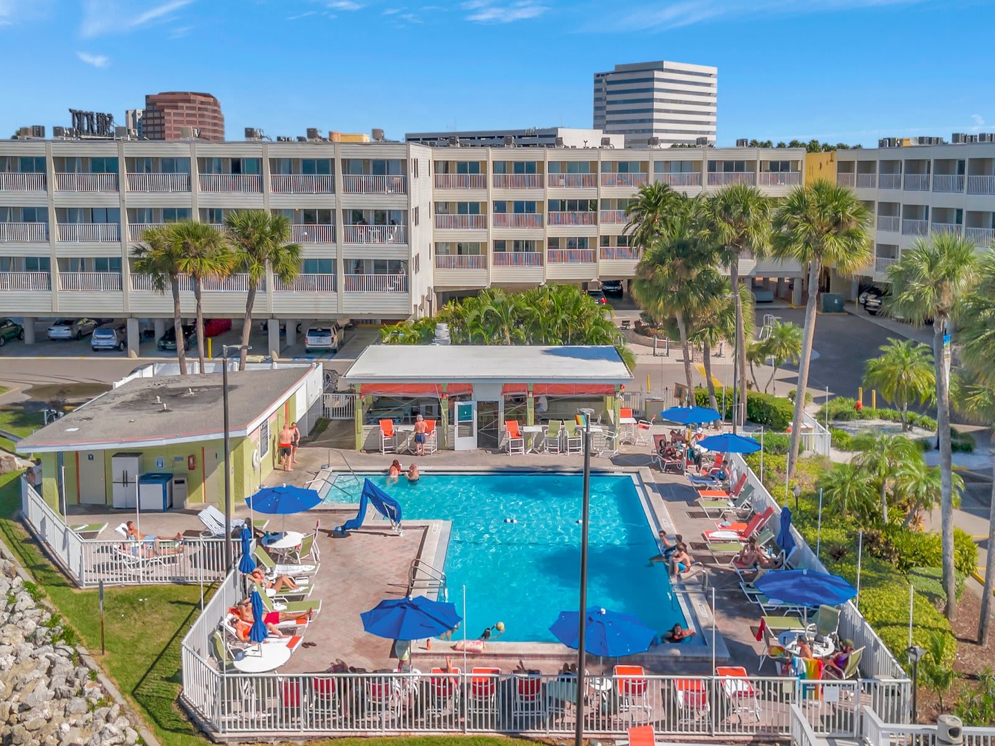 A cheerful waterfront property featuring tropical palm trees, a refreshing pool area with colorful lounge seating, and convenient poolside amenities—all set against a sunny coastal backdrop.