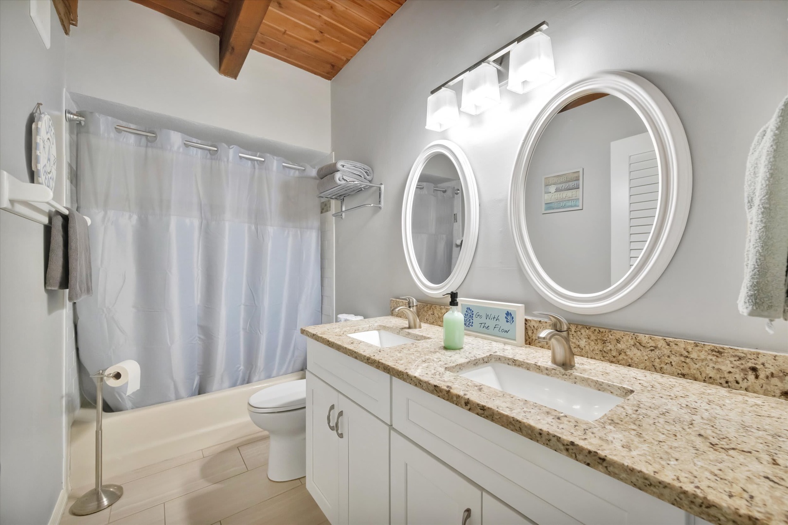 Step into your private bathroom sanctuary with warm wood-beamed ceilings, a dual-sink vanity topped with speckled granite, and a relaxing tub-shower combo ready for you.