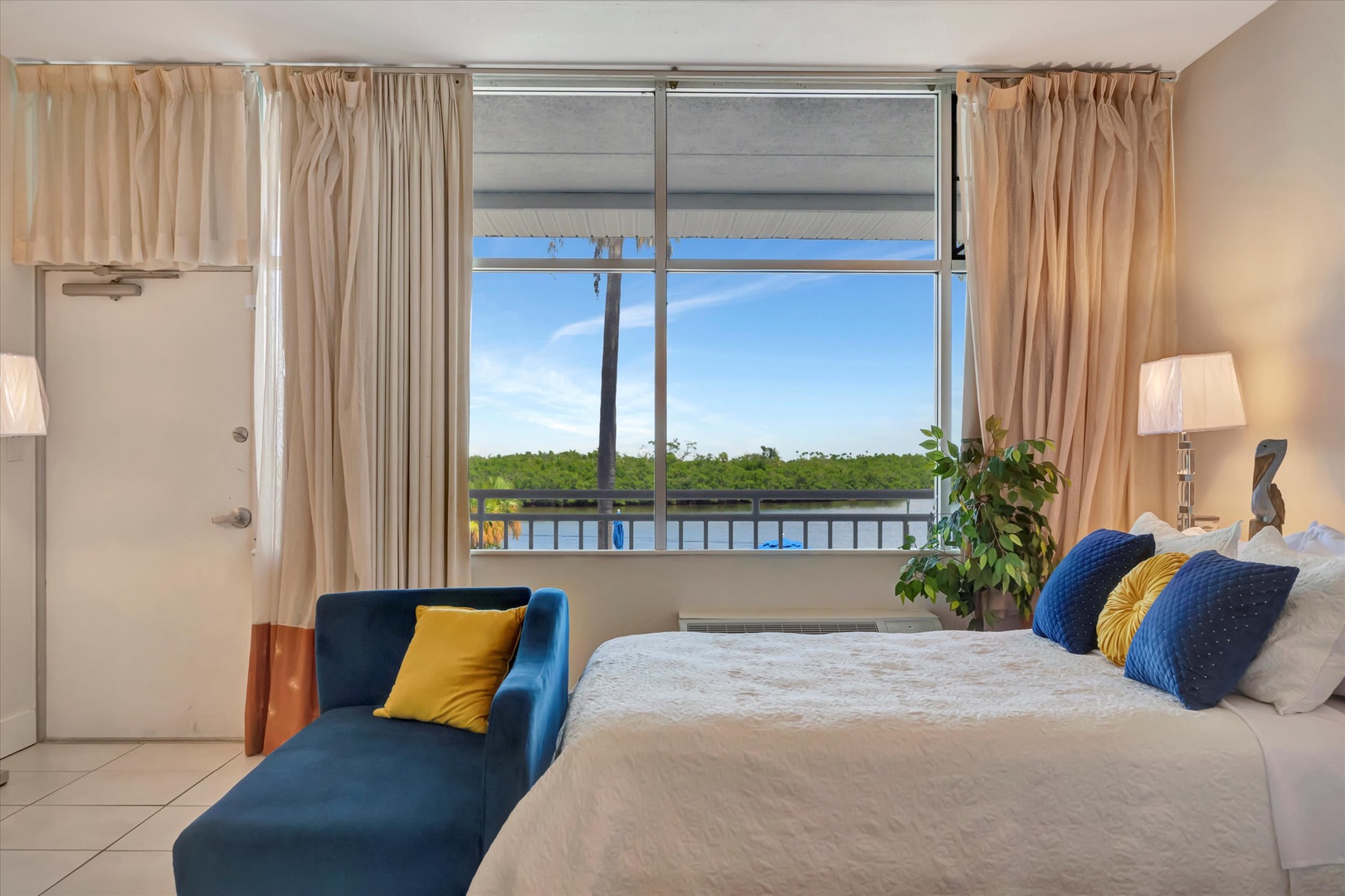 Wake up to a stunning river view framed by your window, where lush greenery meets tranquil waters. Your cozy retreat features a plush bed with vibrant accents and a chic lounge chair—perfect for soaking in the peaceful scenery.
