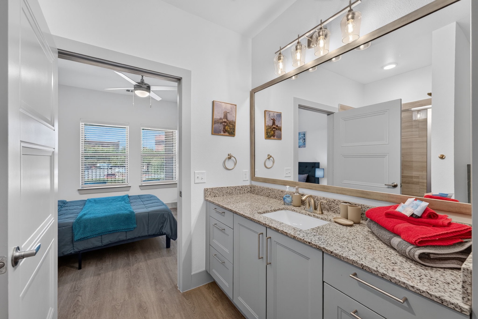 Step into your private bathroom with a stylish vanity and fresh towels waiting. Through the doorway, your peaceful bedroom beckons with natural light streaming in.