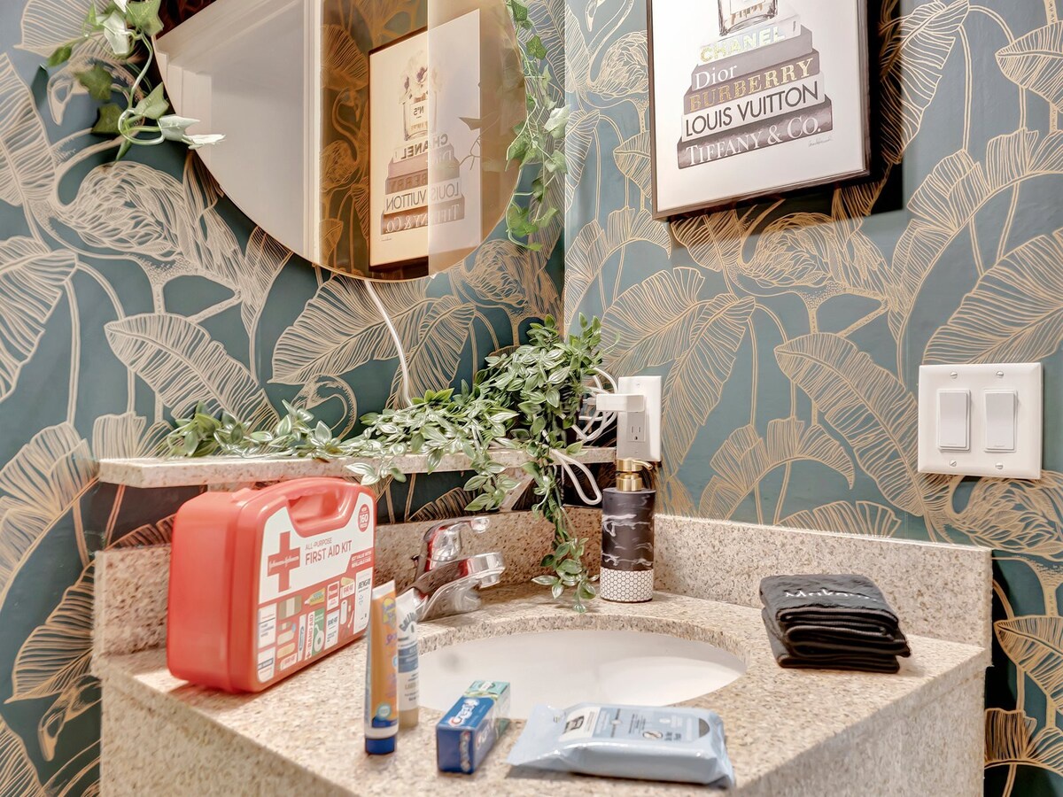 Freshen up in your stylish bathroom with bold tropical wallpaper, plush towels, and thoughtful touches like fresh greenery and luxe framed art.
