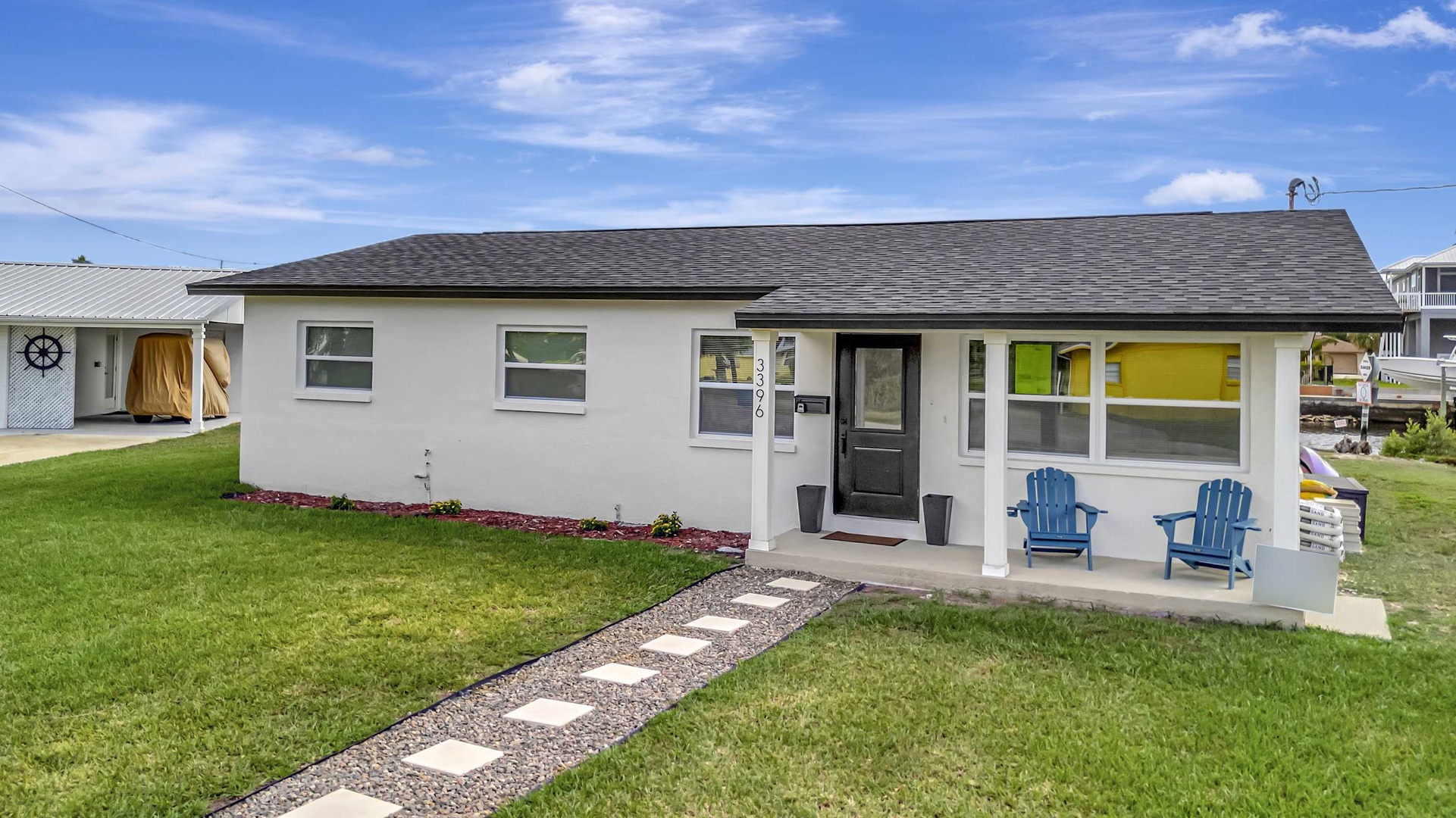 A freshly updated vacation home with a charming front porch and welcoming blue chairs, set in a peaceful neighborhood under bright sunny skies.