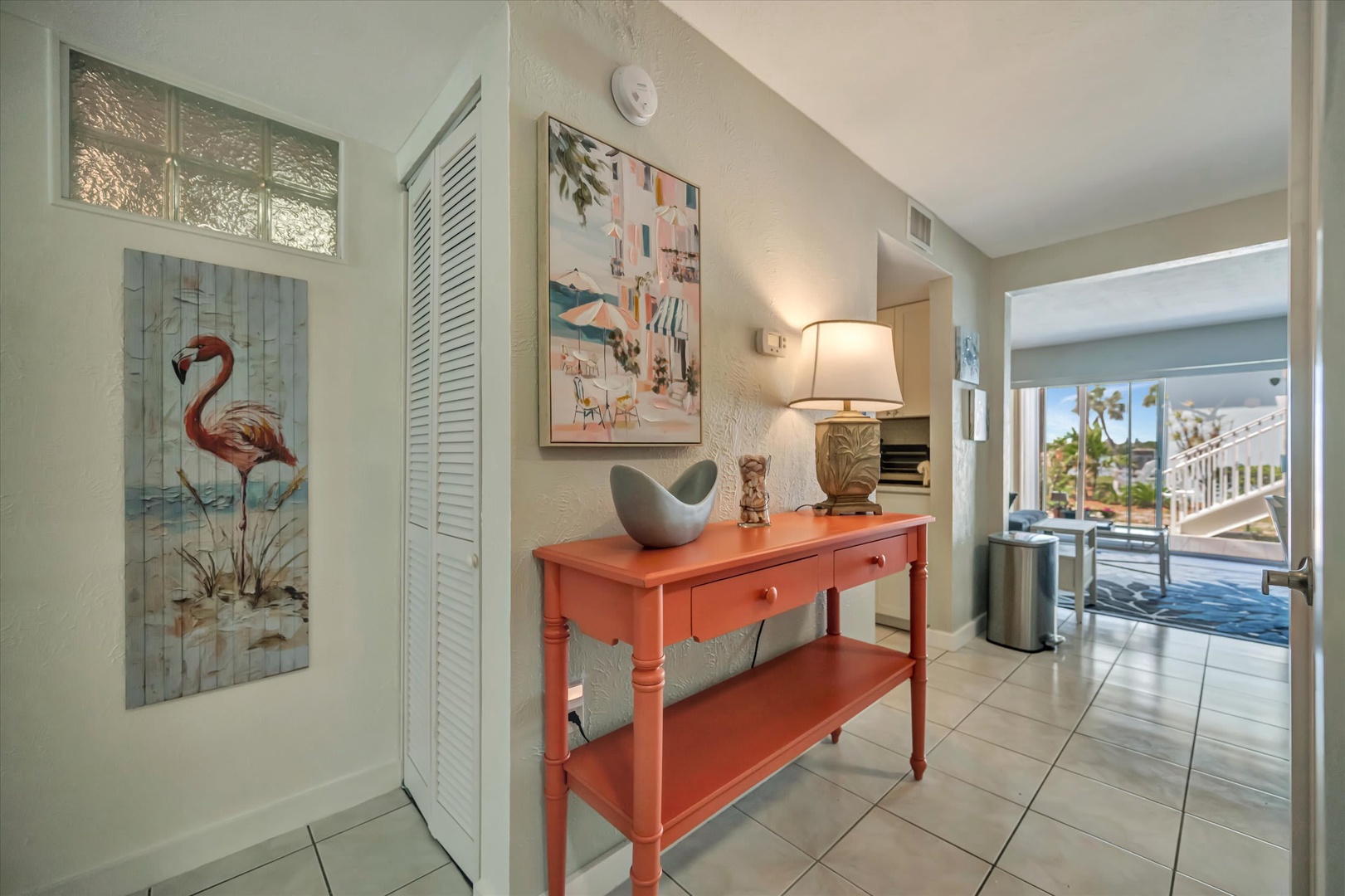 A bright entryway welcomes you with coastal charm—playful flamingo art, fresh white shutters, and a cheerful coral table hint at the relaxing beachy vibe throughout your stay.