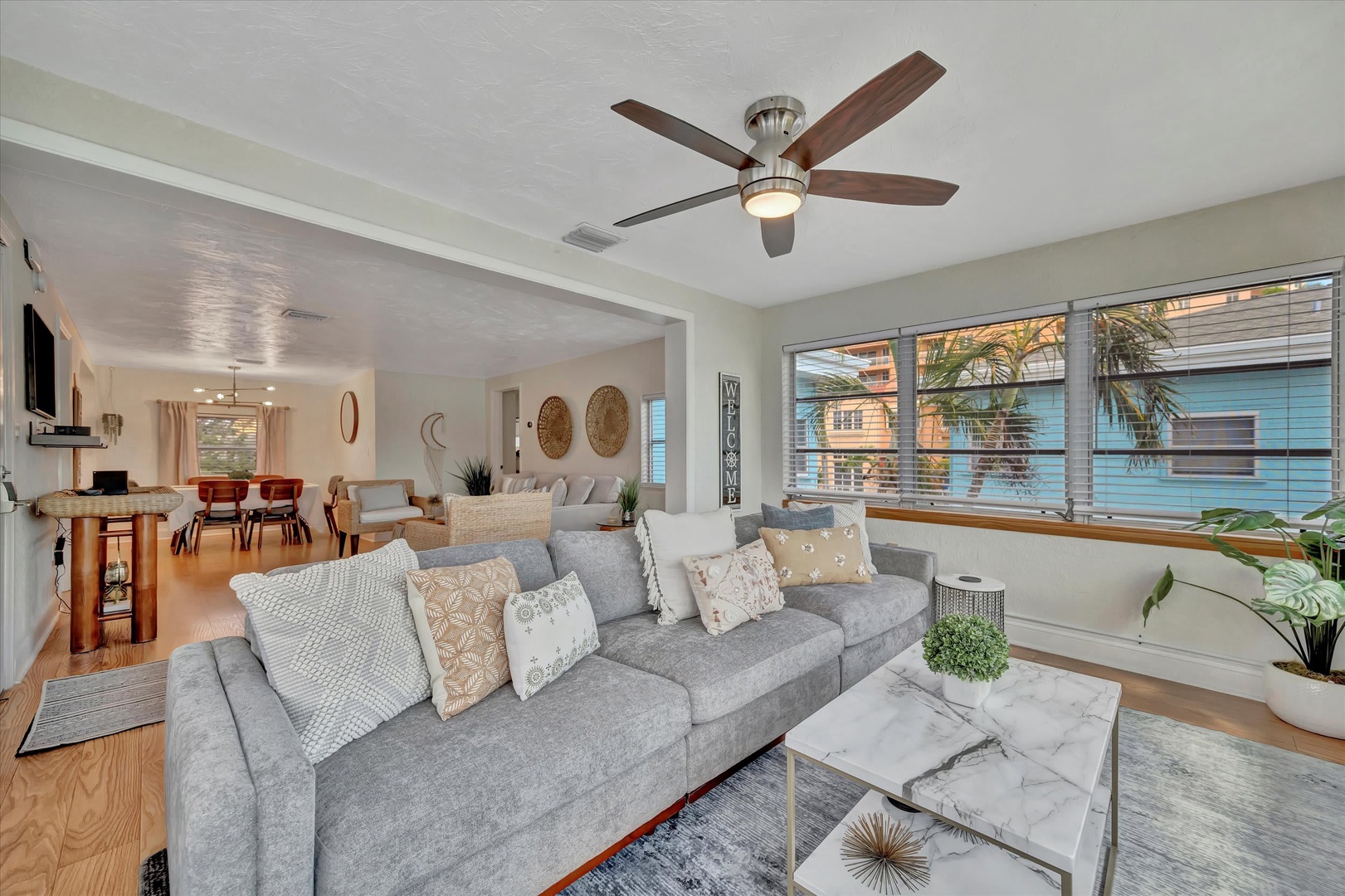 Sink into the plush sofa and feel the coastal breeze from your ceiling fan as natural light streams through the windows, illuminating your bright, open-concept living space.
