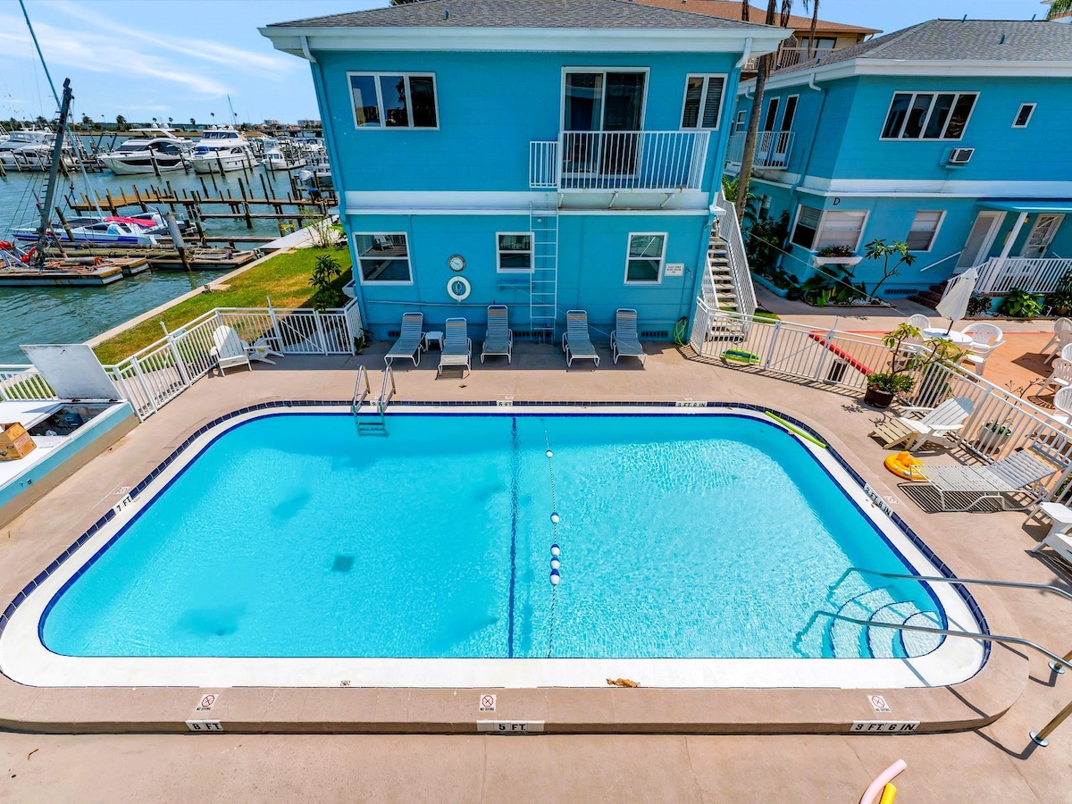 Bright turquoise buildings frame a sparkling pool with marina views, where your days unfold between waterside lounging and coastal exploration.