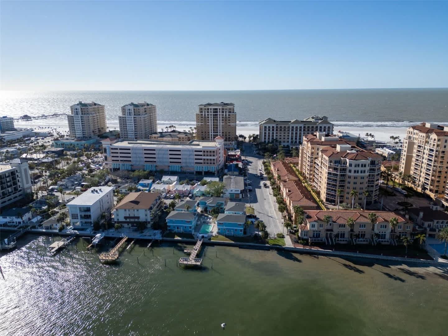 The property is located in a vibrant beachfront community with marina access, high-rise condos, and sandy shores stretching along the coast.