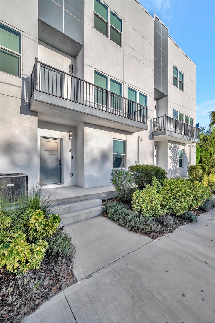 Modern townhome entry framed by manicured landscaping and sunlit walkways. A welcoming first impression in a peaceful residential setting.