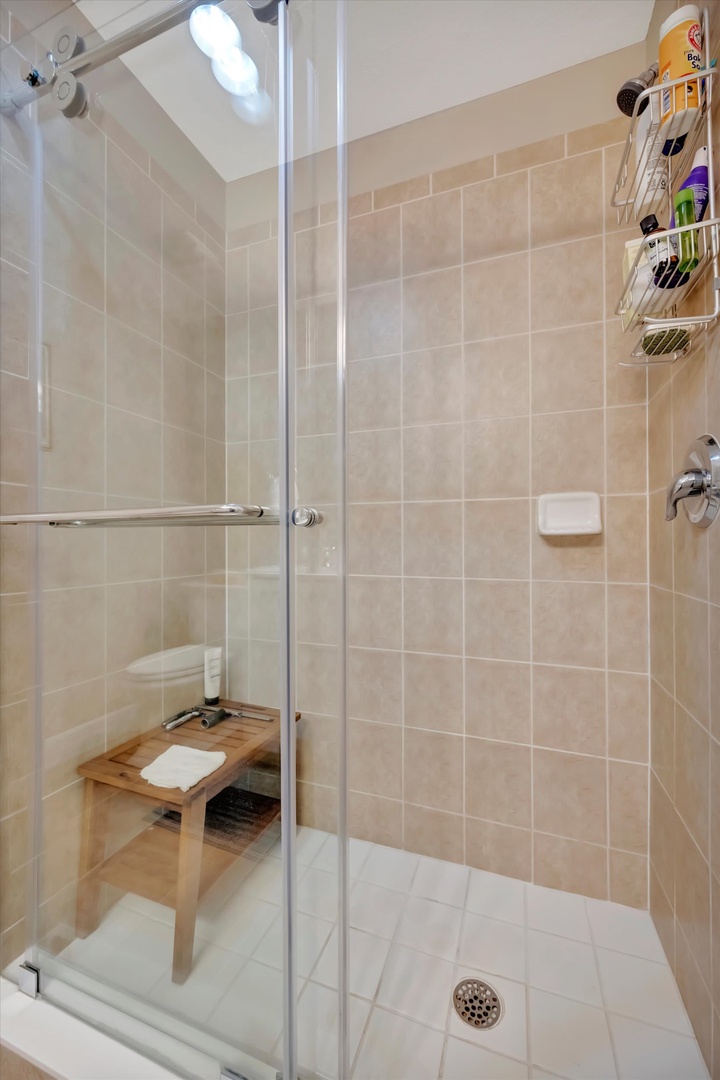 Step into your bright, tiled walk-in shower with a convenient bench and handy caddy stocked with essentials. The skylight above bathes the space in natural light.