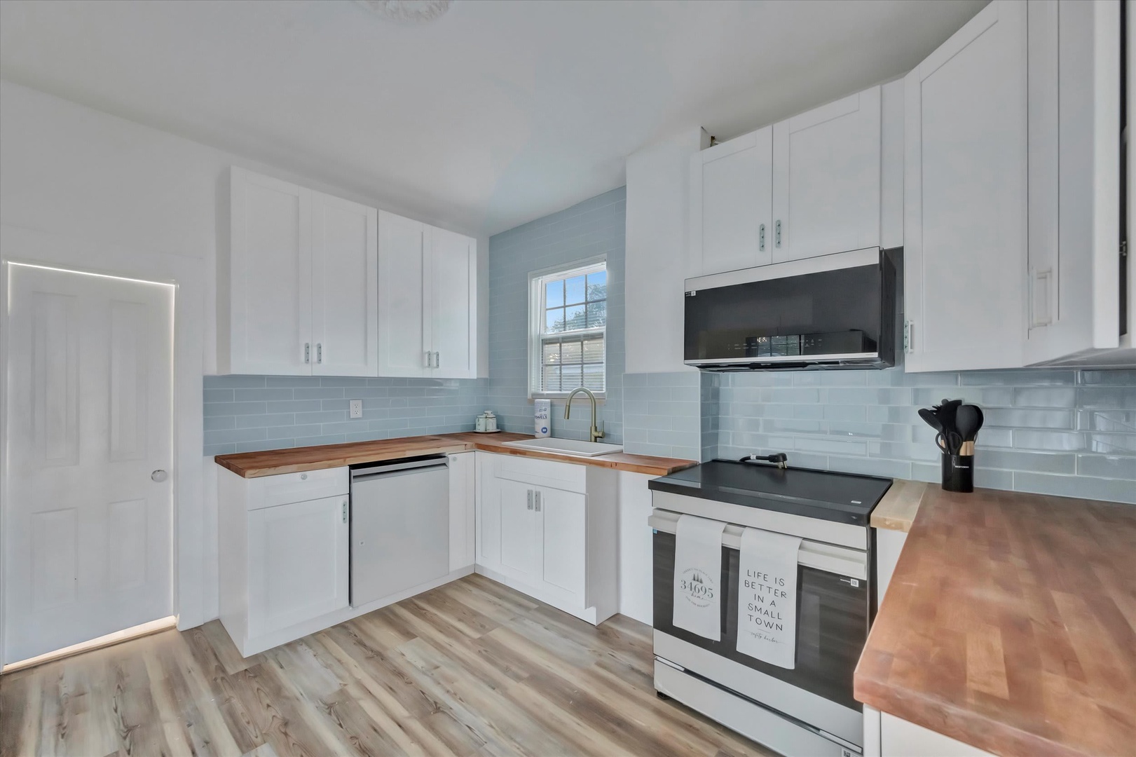 Step into your bright, fully-equipped kitchen with warm butcher-block counters, sleek white cabinetry, and soothing blue subway tile. Everything you need to cook up your favorite meals awaits.