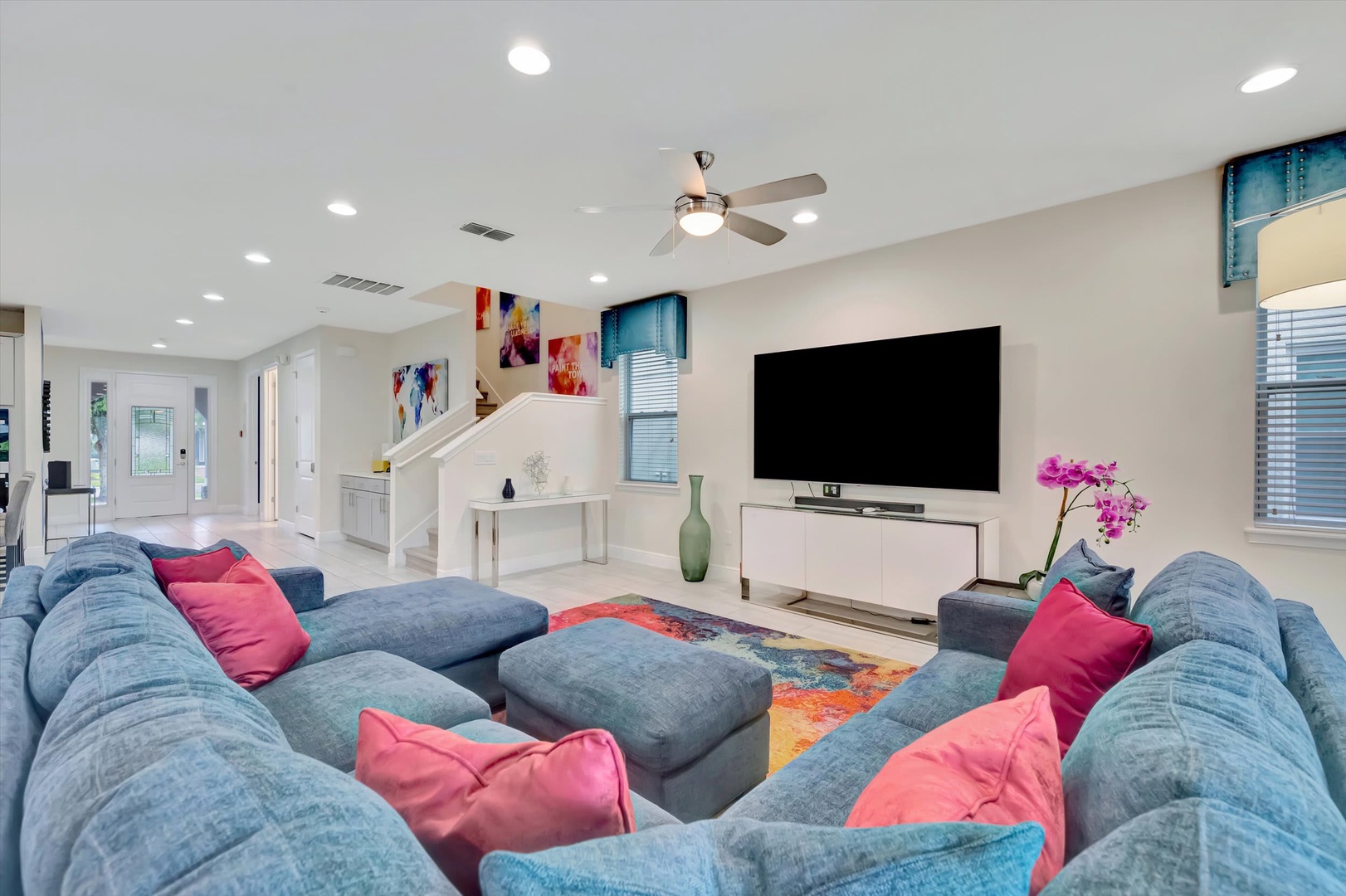 Sink into plush blue sectionals with vibrant coral pillows in your spacious living room, where natural light and modern comforts create the perfect spot to unwind together.