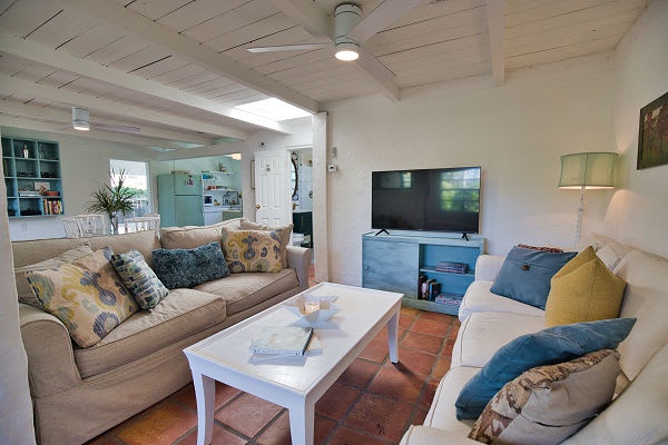 Step into your bright, airy living space where coastal vibes meet home comfort—soft couches invite you to unwind, and the open-plan kitchen beckons you to gather and share stories after sun-filled days.