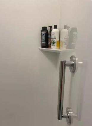 Your shower stall features a sleek corner shelf stocked with premium bath amenities, plus a modern stainless steel grab bar for your comfort and safety.