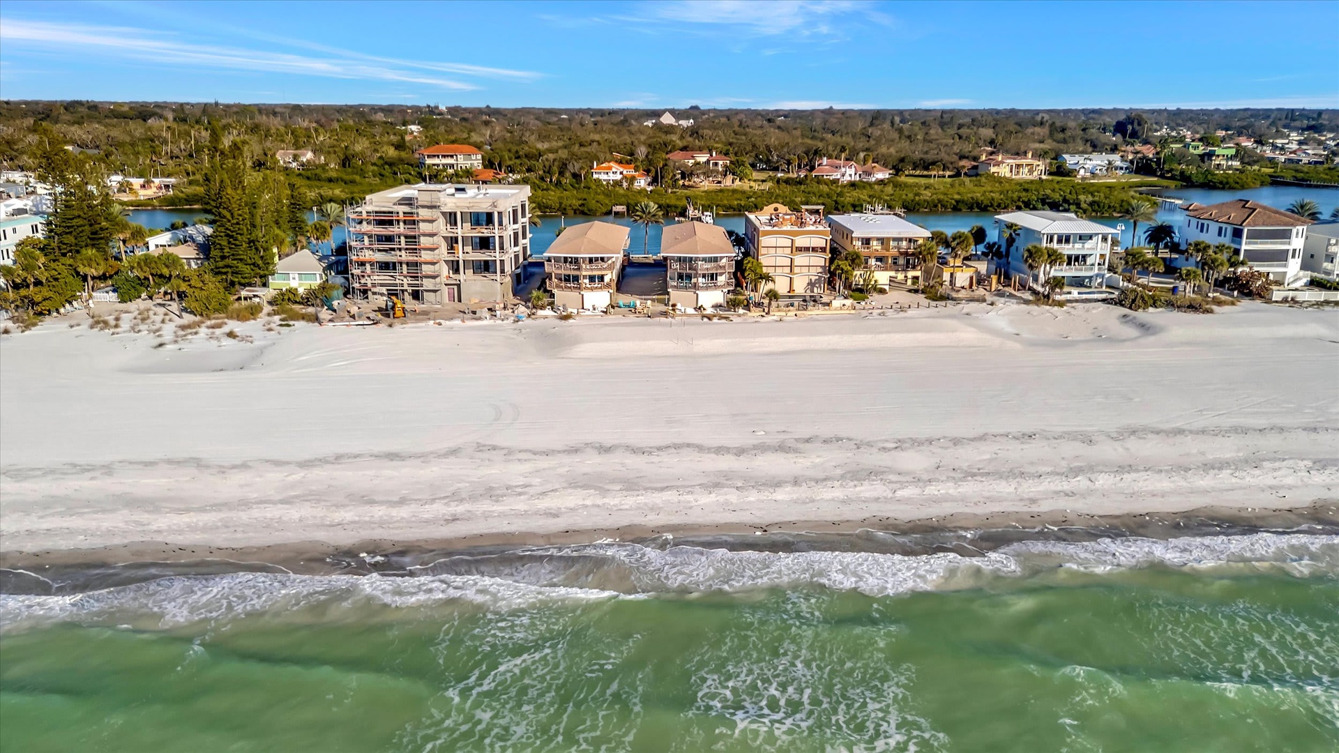 Aerial view showcasing the beachfront property location along pristine white sand and turquoise waters, with nearby waterfront homes and natural landscapes.