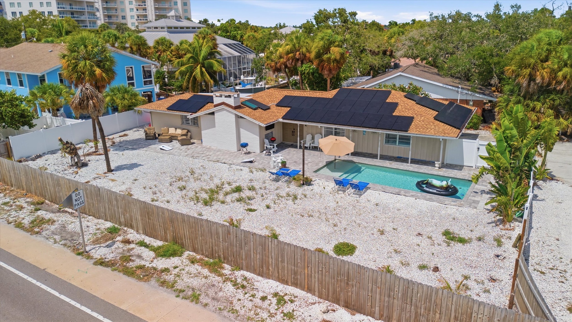 Aerial view of a spacious beachside property with private pool and covered patio, surrounded by palm trees and tropical landscaping in a relaxed coastal neighborhood.